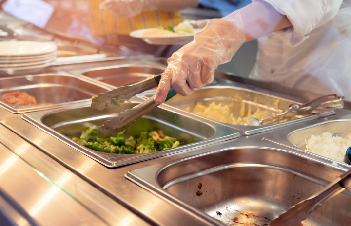 A person serves food onto a plate at a buffet, showcasing a variety of dishes and a vibrant dining atmosphere