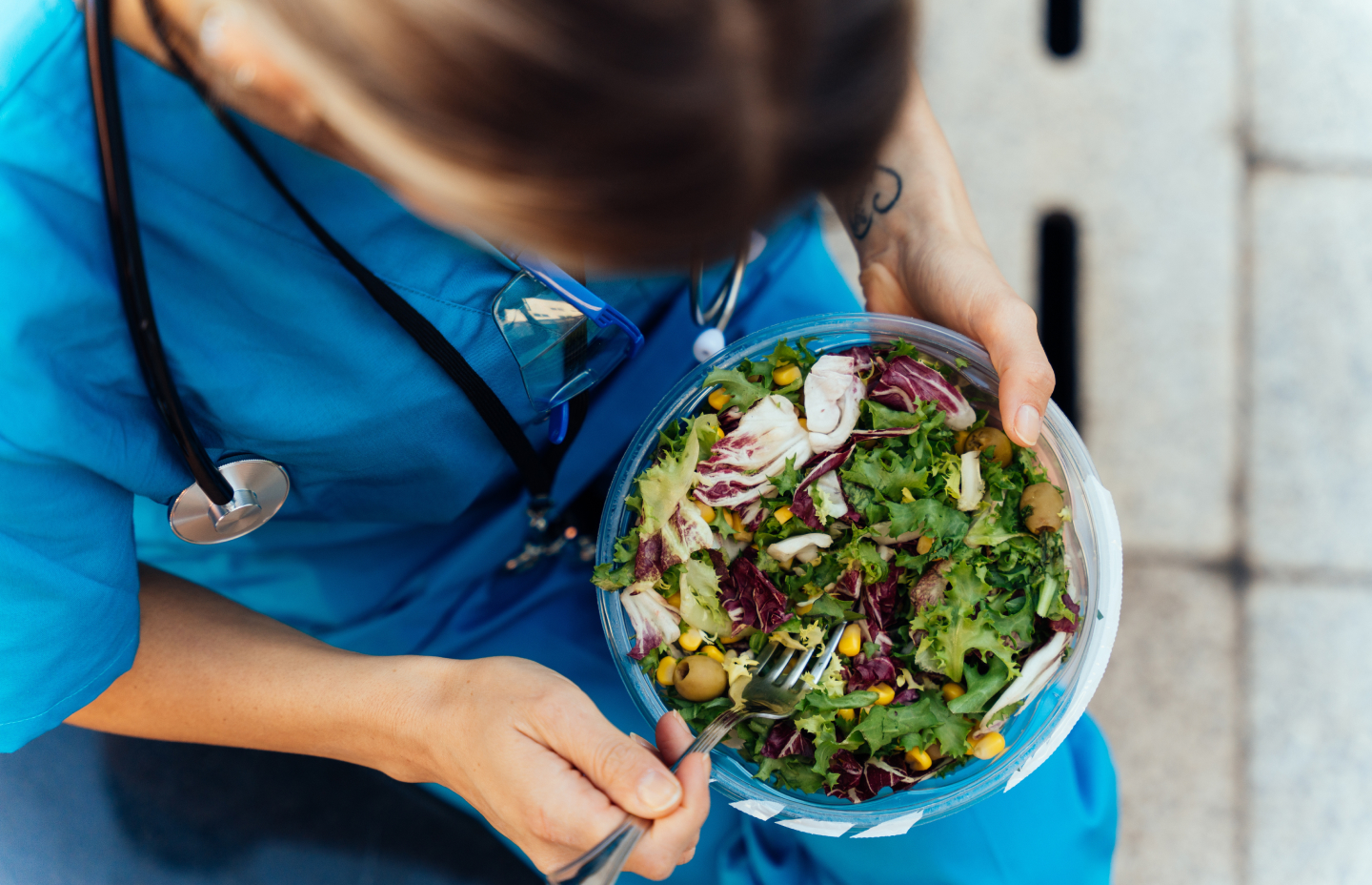 A woman in a blue uniform holds a fresh salad, showcasing a healthy meal choice in a casual setting