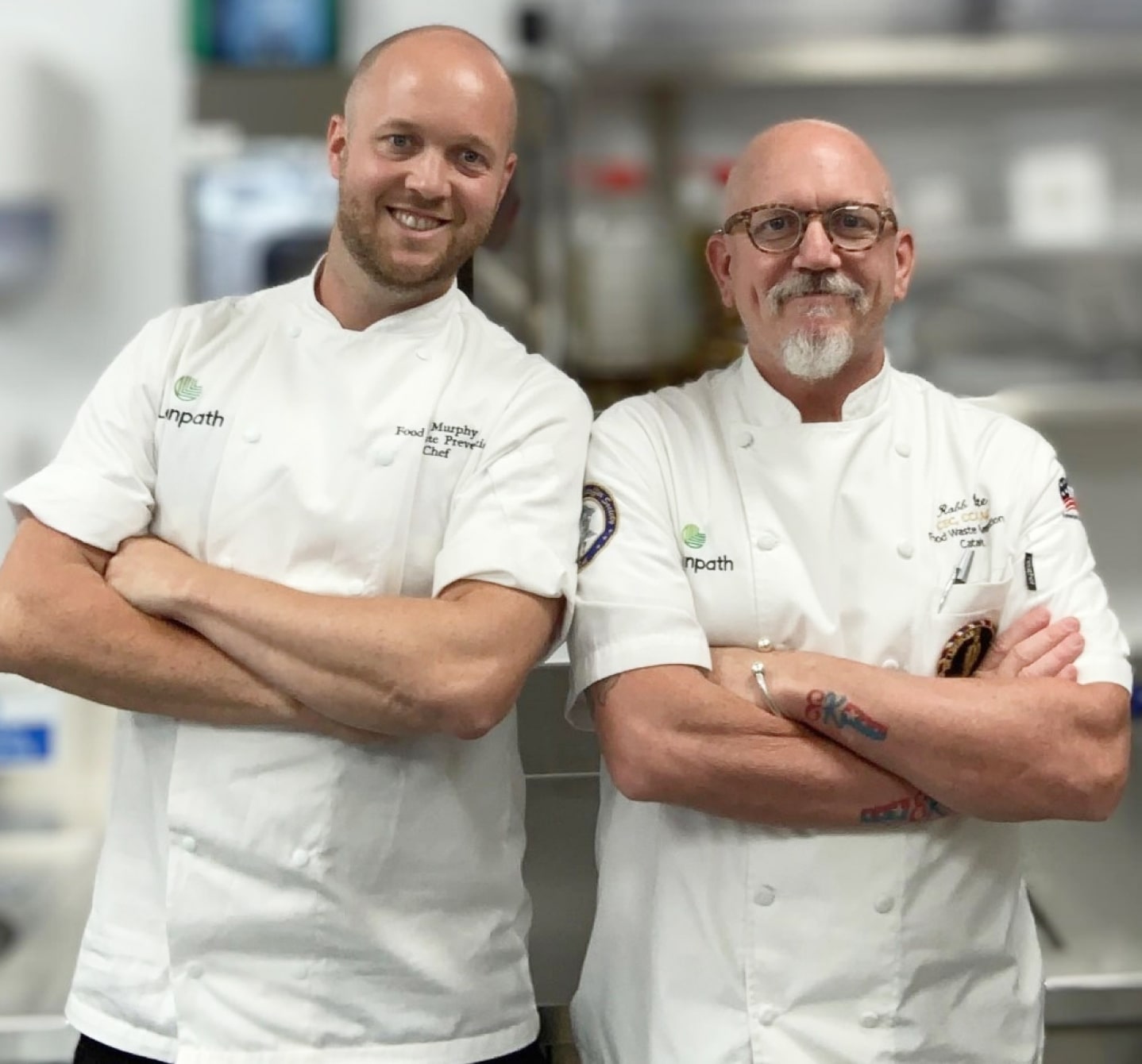 Two chefs in a kitchen, standing confidently with arms crossed, showcasing a professional and collaborative atmosphere