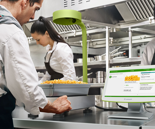 Artichokes are displayed on the background, a man and woman collaborate in a kitchen, utilizing a computer and monitor for their tasks