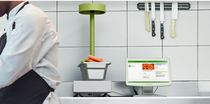 A man dressed in an apron stands adjacent to a computer