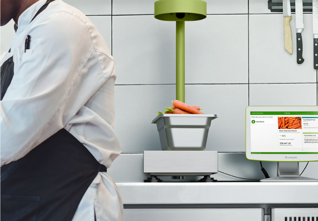 A man dressed in an apron stands adjacent to a computer