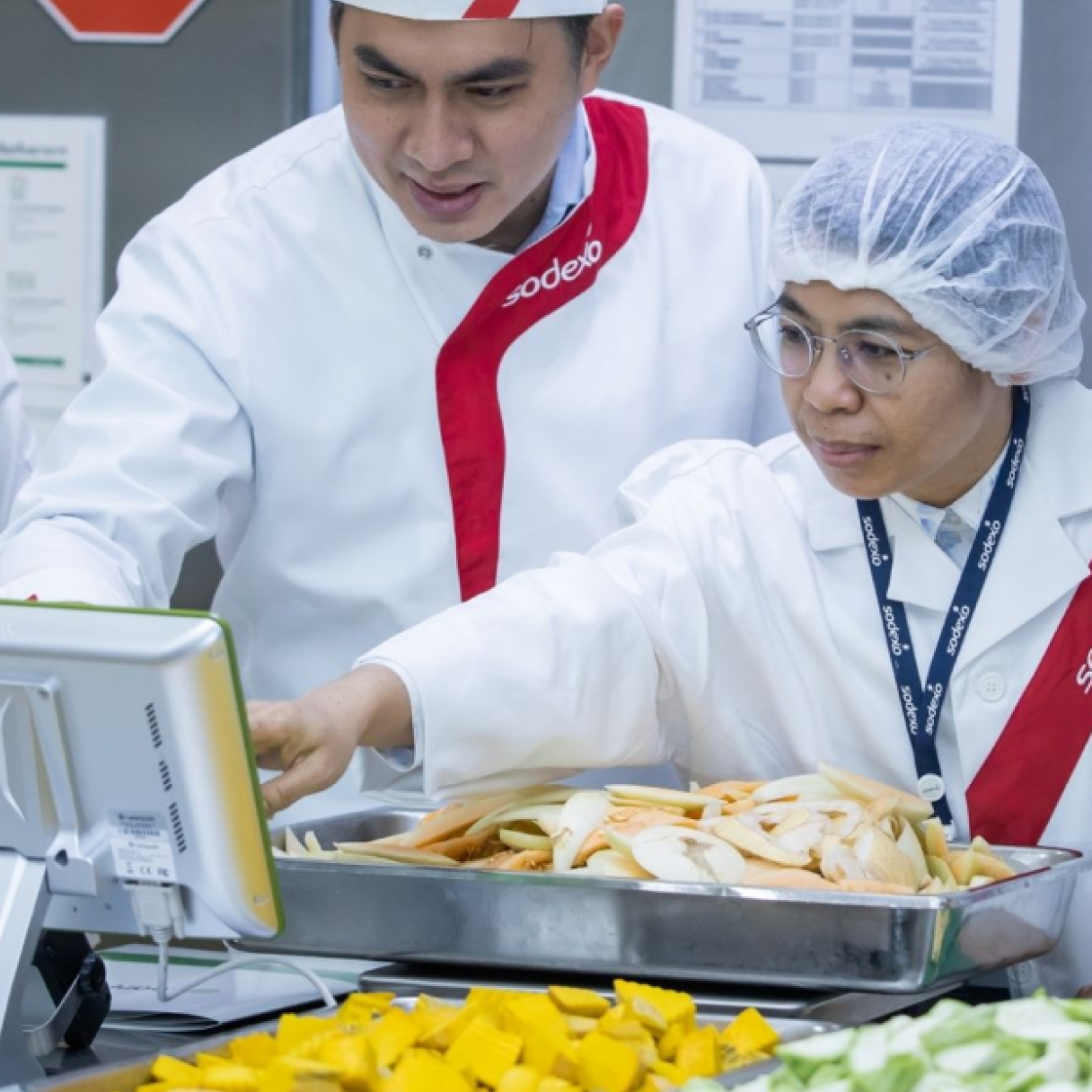 Two people dressed in white uniforms attentively observing food arranged on a tray, highlighting their professional engagement