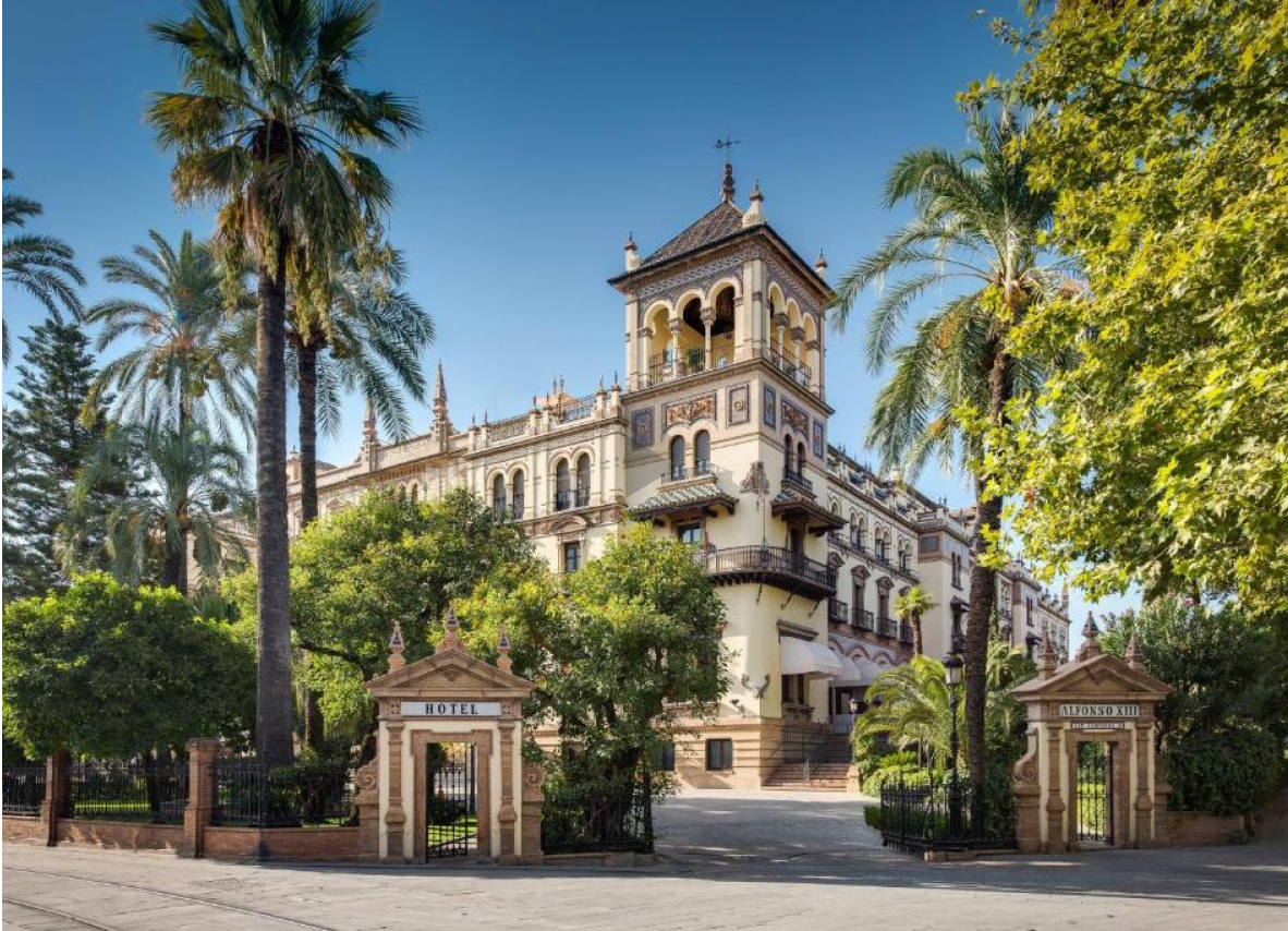 A building featuring palm trees in the foreground and a prominent clock tower against a clear sky