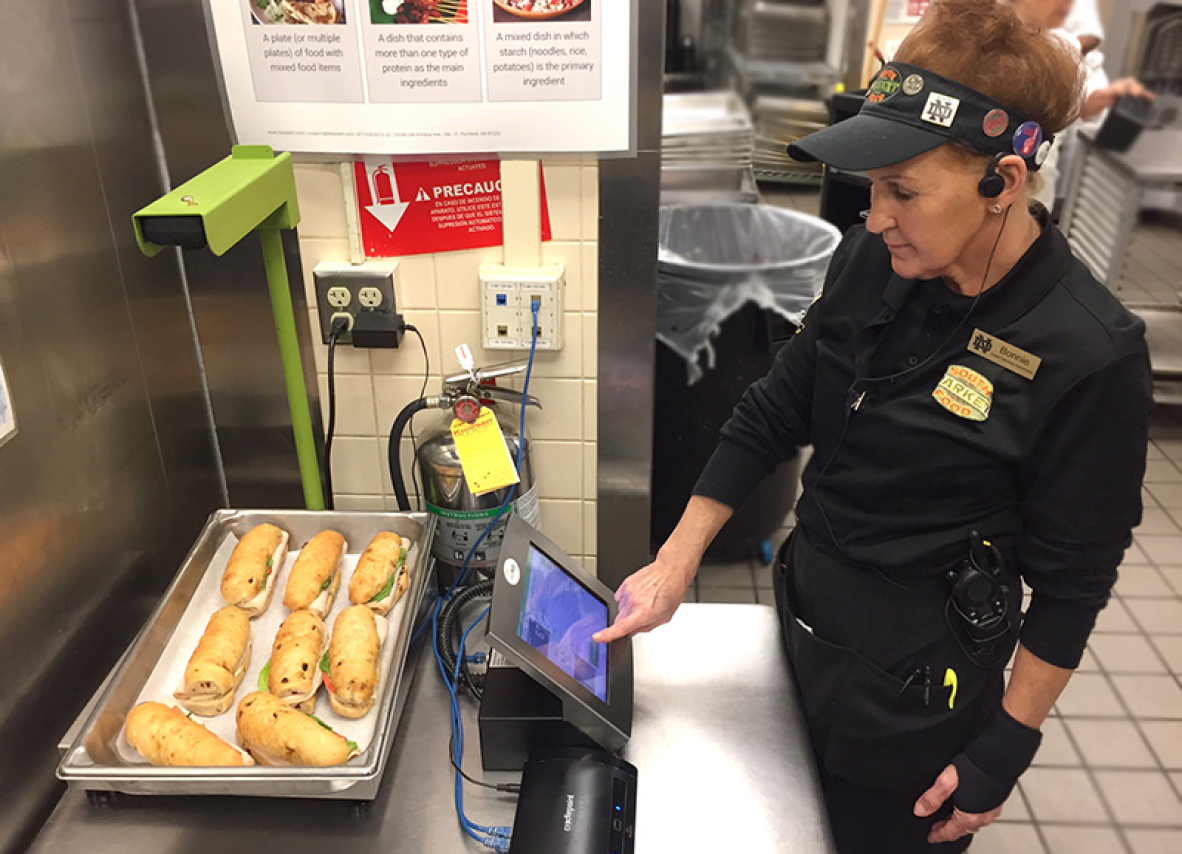 A uniformed woman stands next to a tray of sandwiches