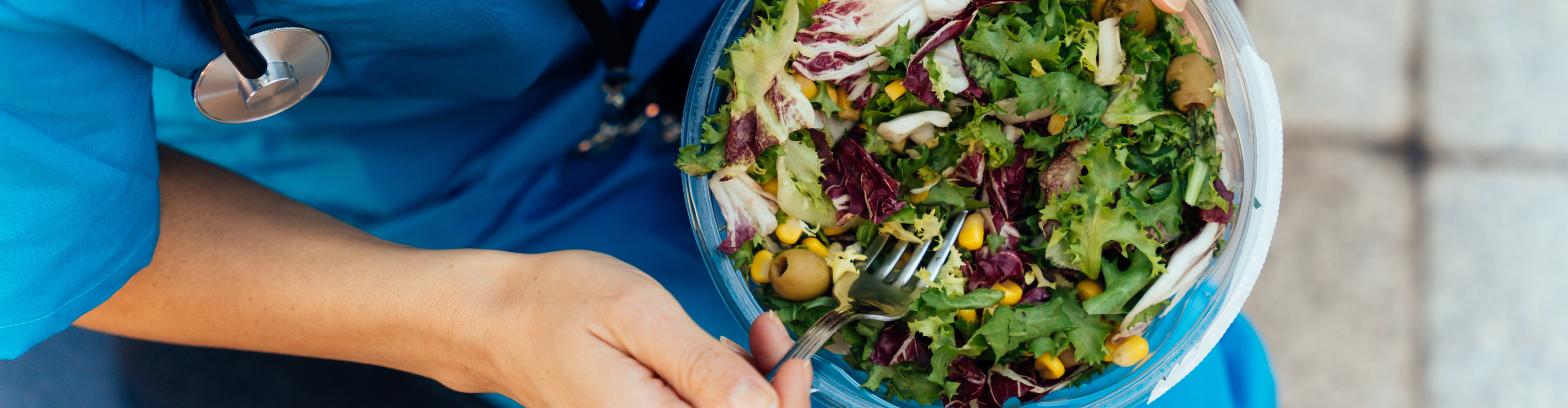 A woman in a blue uniform holds a fresh salad