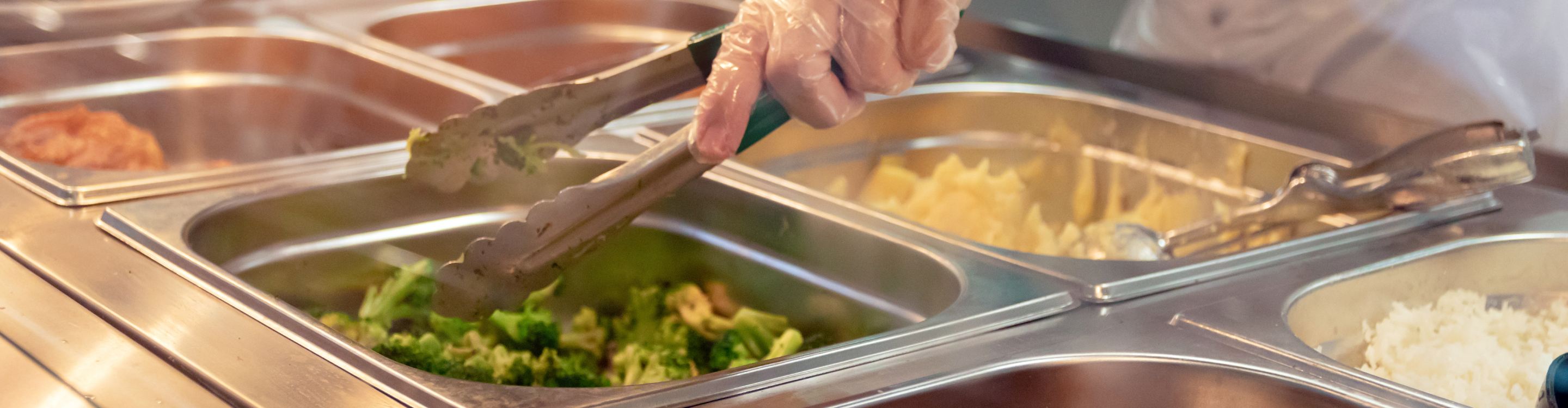 A person serves food onto a plate at a buffet, showcasing a variety of dishes and a vibrant dining atmosphere