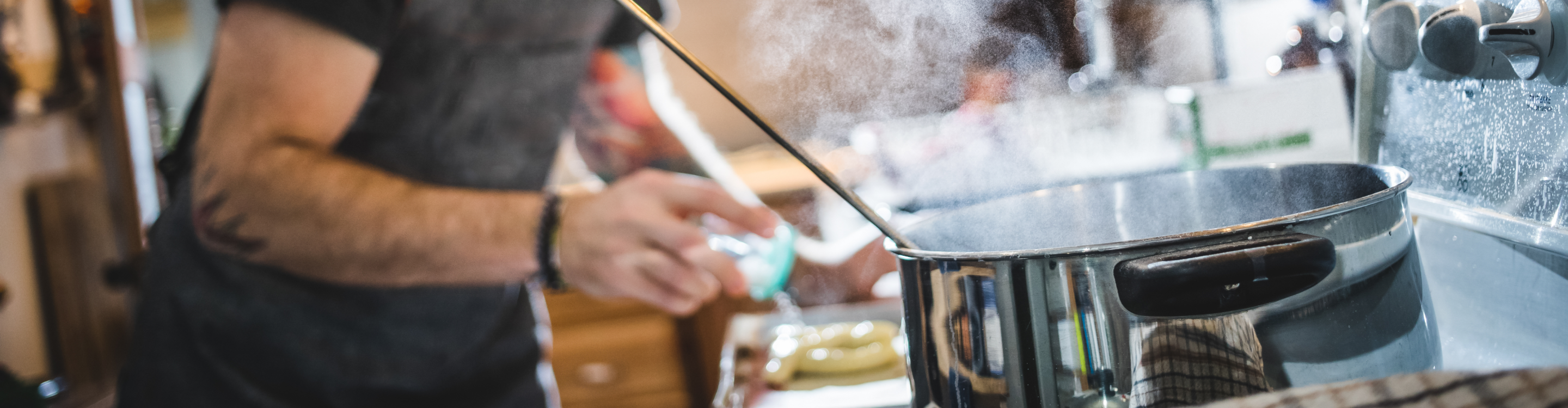 A man wearing an apron is skillfully cooking in a well-equipped kitchen, surrounded by various cooking utensils and ingredients