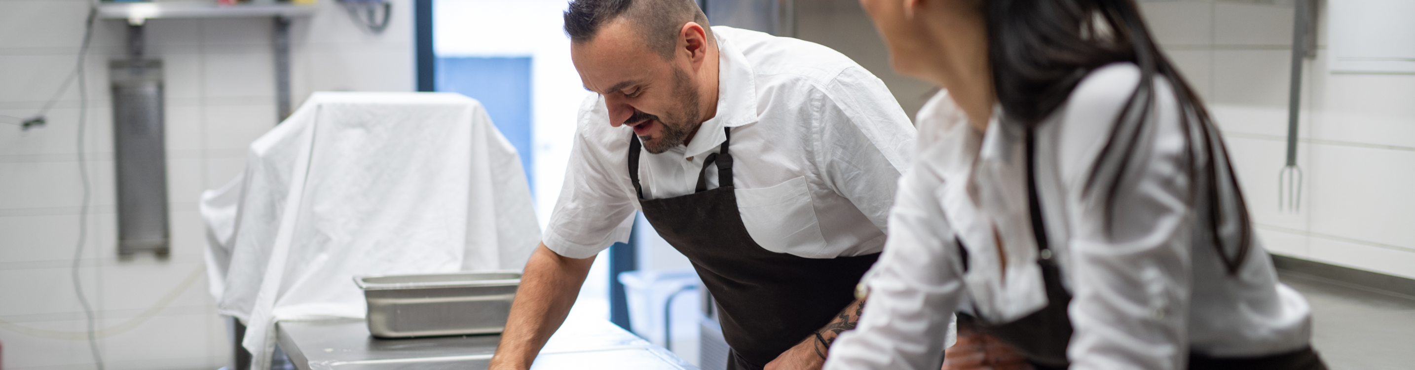 A man and woman in a uniform collaborate in a kitchen, engaged in cooking and preparing a meal together