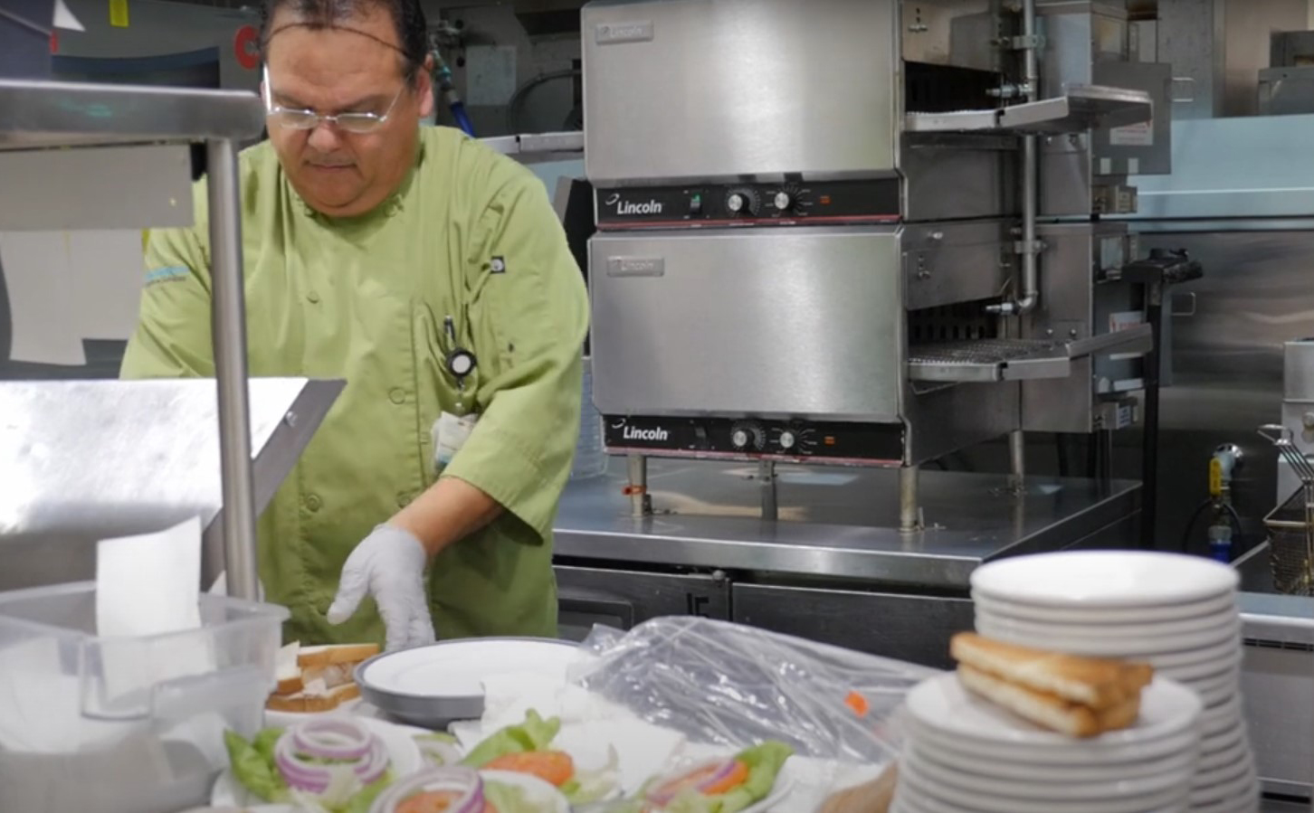 A man in a green uniform skillfully prepares food in a well-equipped kitchen, showcasing culinary expertise and focus