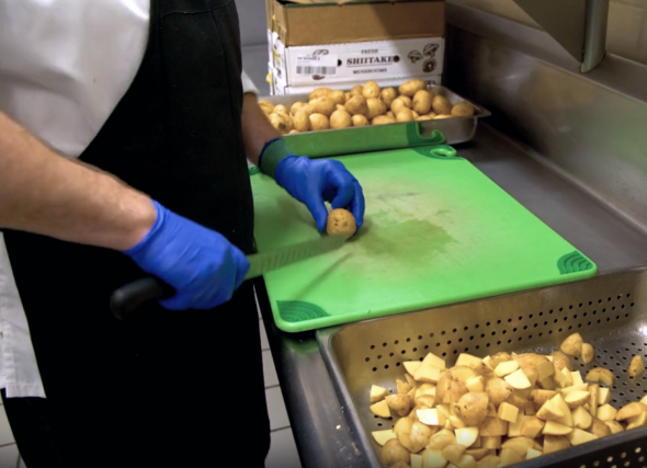 A person skillfully cuts potatoes on a wooden cutting board in a well-lit kitchen