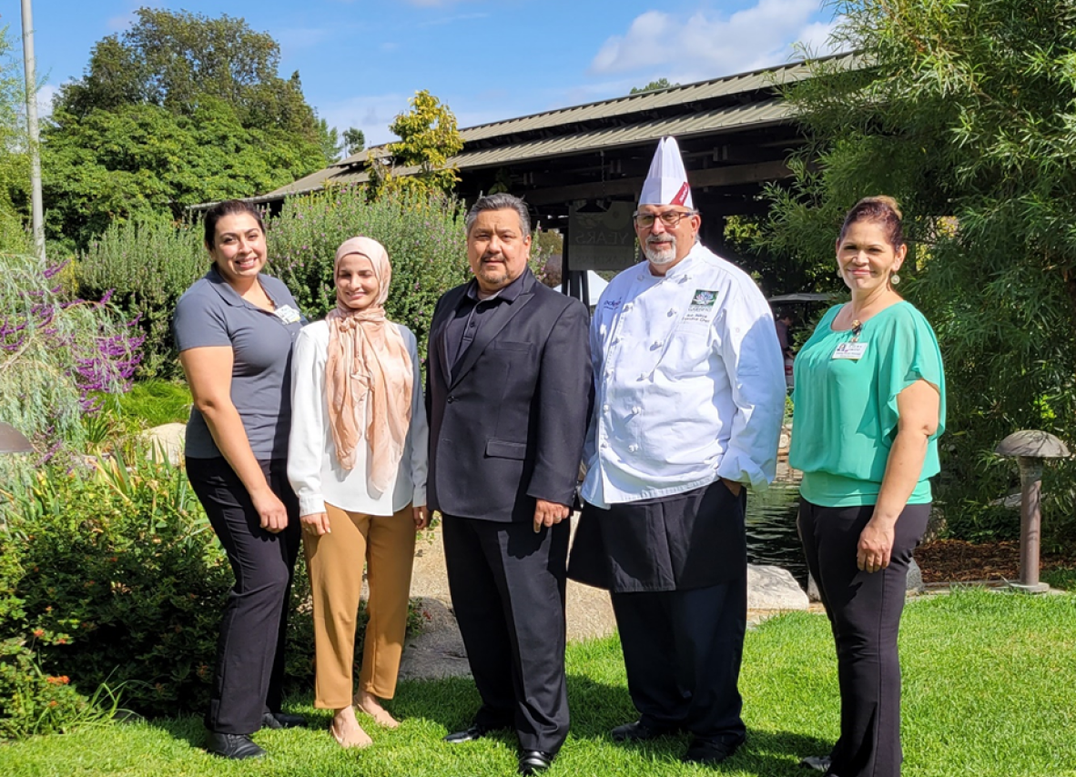 A diverse group of individuals stands together in front of a vibrant garden